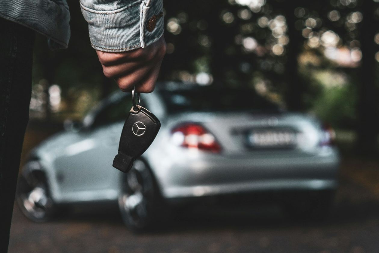 Autosleutel in de hand met de auto op de achtergrond
